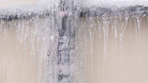 Winter Effects on Drain Pipes – Exterior drain pipes covered in thick ice and icicles, showing severe freezing during winter weather.